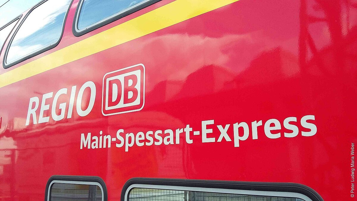 Main Spessart Express Seitenansicht eines roten Zuges mit der Aufschrift „Regio DB Main-Spessart-Express“ und gelbem Streifen oberhalb.